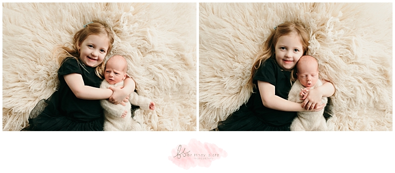 Big sister cuddling baby brother on white flokati